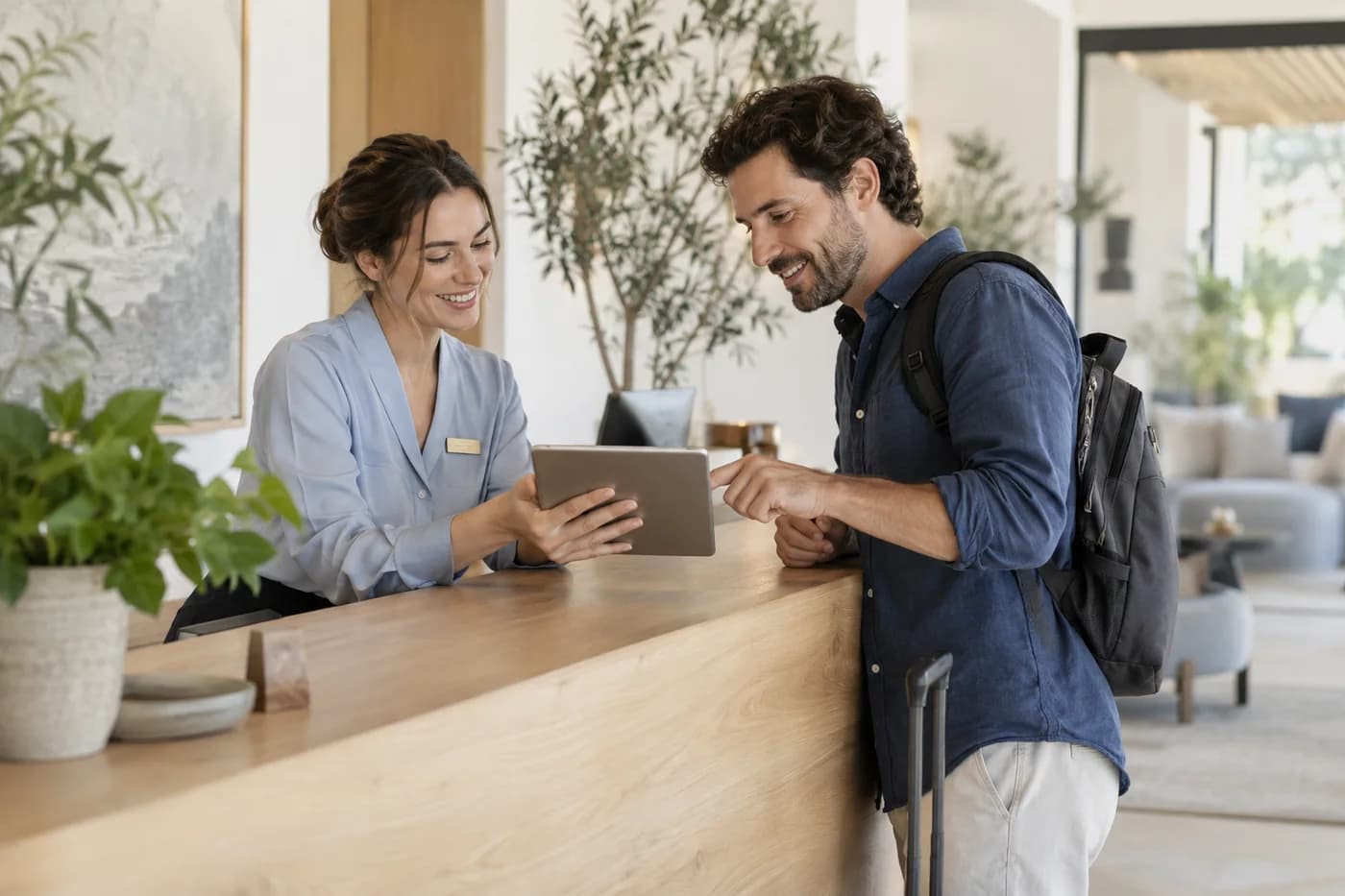 A hotel receptionist and traveler reviewing booking details at the front desk.